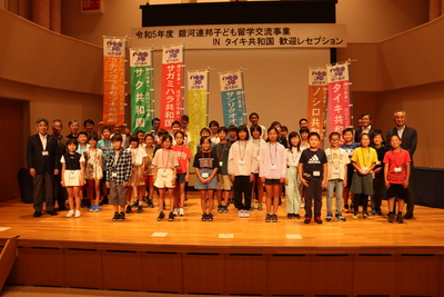それぞれ色の違う各共和国ののぼりの前に集合した参加児童と関係者の、ステージ上での集合写真