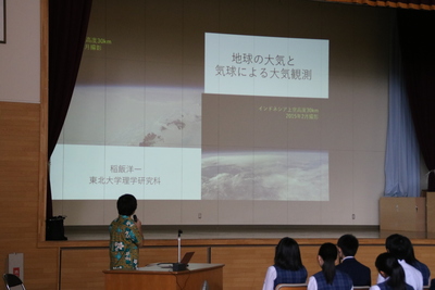 体育館のステージ上でスライドショー形式にて進行する、「地域人材を活用した講演会」（演題：地球と大気と気球による大気観測）の講演風景の写真