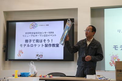 SORAの集会室にて、モデルロケットの製作キットを手にしつつレクチャーを行う講師の写真