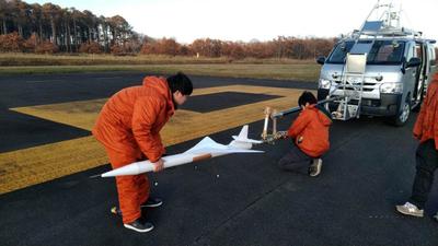 滑走路上にてオオワシ2号の縮小機体を持ち運ぶスタッフ2名の写真