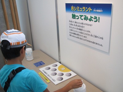 月のシミュラントコーナーで月の砂の成分を模した模擬砂に触れてみる児童の写真